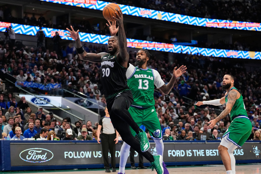 Minnesota Timberwolves forward Julius Randle (30) leaps to the basket for a shot after getting past Dallas Mavericks' Naji Marshall (13) and Caleb Martin, right, in the first half of an NBA basketball game Wednesday, Jan. 28, 2026, in Dallas. (AP Photo/Tony Gutierrez)