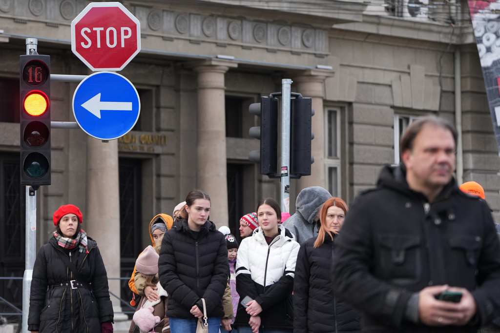 People stand in silence to commemorate the 16 victims, killed after a railway concrete canopy fell in Nov. 2024 while Serbia's protesting university students collect signatures throughout the country for their request for an early parliamentary election, in Belgrade, Serbia, Sunday, Dec. 28, 2025. (AP Photo/Darko Vojinovic)