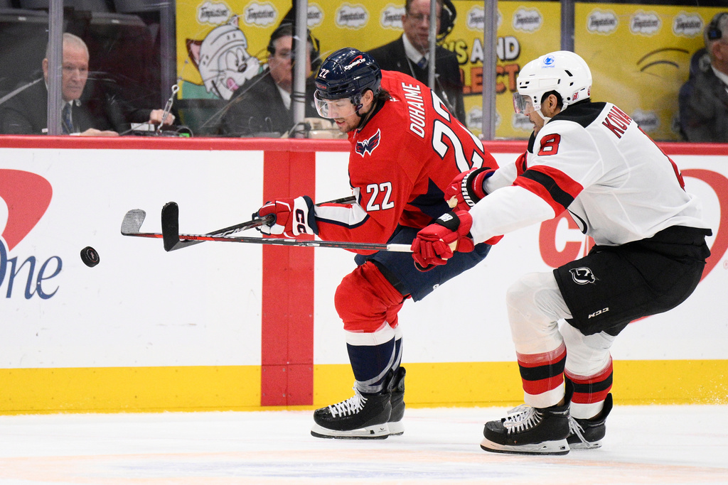 Washington Capitals left wing Brandon Duhaime (22) and New Jersey Devils defenseman Johnathan Kovacevic (8) chase the puck during the second period of an NHL hockey game Friday, March 20, 2026, in Washington. (AP Photo/Nick Wass)