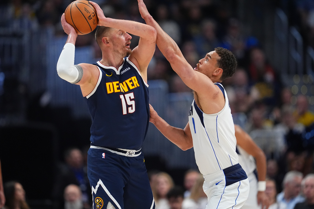 Denver Nuggets center Nikola Jokić, left, looks to pass the ball as Dallas Mavericks forward Dwight Powell defends in the first half of an NBA basketball game Wednesday, March 25, 2026, in Denver. (AP Photo/David Zalubowski)