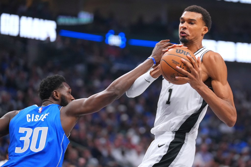 San Antonio Spurs forward Victor Wembanyama, right, tries to control the ball after a rebound as Dallas Mavericks center Moussa Cisse tries to disrupt him during the first half of an NBA basketball game Saturday, Oct. 24, 2026, in Dallas. (AP Photo/Julio Cortez)