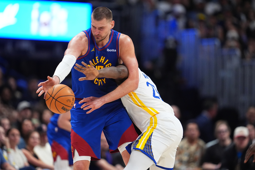 Denver Nuggets center Nikola Jokić, left, struggles to field a pass as Golden State Warriors forward Draymond Green defends in the second half of an NBA basketball game Sunday, March 29, 2026, in Denver. (AP Photo/David Zalubowski)