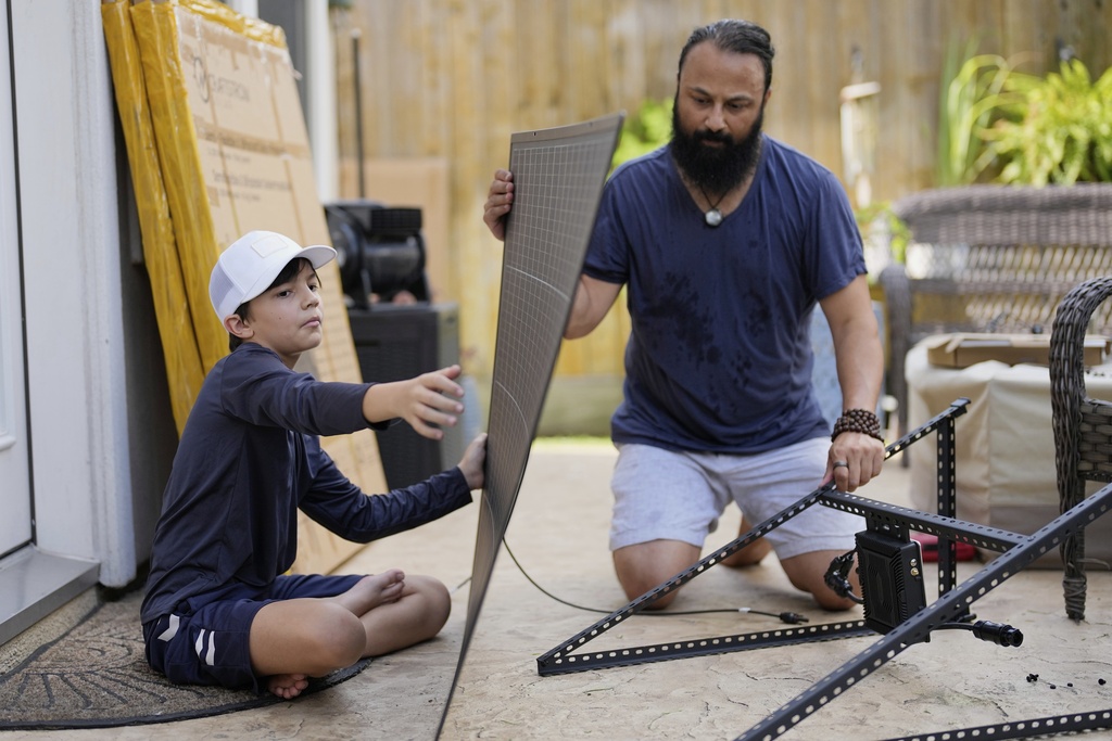 Bhavin Misra, right, and his son, Rumi, 10, assemble a Craftstrom Solar plug-in kit at their home Tuesday, Aug. 5, 2025, in Houston. (AP Photo/David J. Phillip)