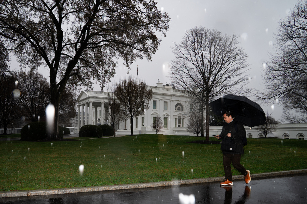A person walks through falling snow at the White House on Thursday, March 12, 2026, in Washington. (AP Photo/Allison Robbert)