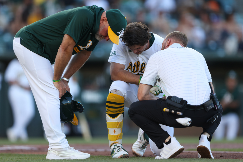 Athletics' Nick Kurtz, center, kneels on the ground while being looked at by the trainer after being hit by the pitch during the first inning of a baseball game against the Boston Red Sox Wednesday, July 29, 2026, in West Sacramento, Calif. (AP Photo/Scott Marshall)
