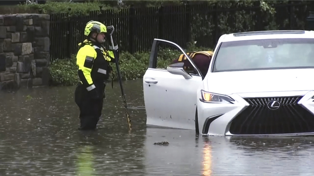This image taken from video shows authorities inspecting a car lying half-submerged in water on a Philadelphia street on Sunday, July 12, 2026 after a line of severe, short thunderstorms passed through the city the day before. (WPVI-TV/6ABC via AP)