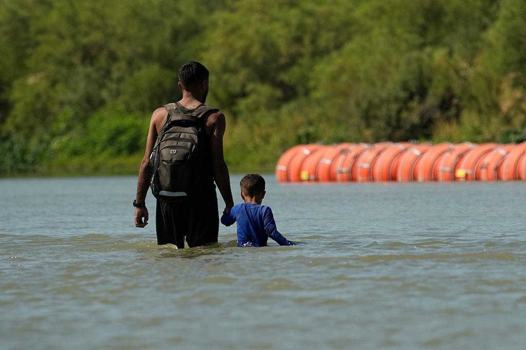 FILE - Migrants walk past large buoys being used as a floating border barrier on the Rio Grande, Aug. 1, 2023, in Eagle Pass, Texas. (AP Photo/Eric Gay, File)