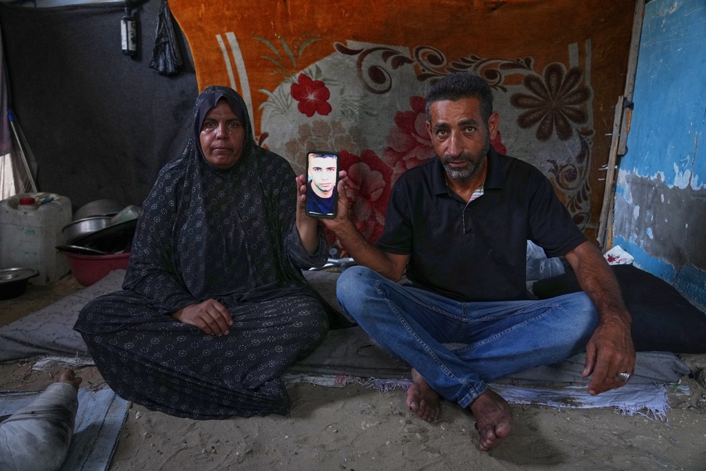 Mohammad and Tahani al-Najjar hold a cellphone showing a picture of their son, Ahmad, at their family's tent in Muwasi, along Gaza's southern coast, Feb. 22, 2025. Nearly two years after Ahmad went missing following Israeli bombardment, the al-Najjars are still searching for him. (AP Photo/Jehad Alshrafi)