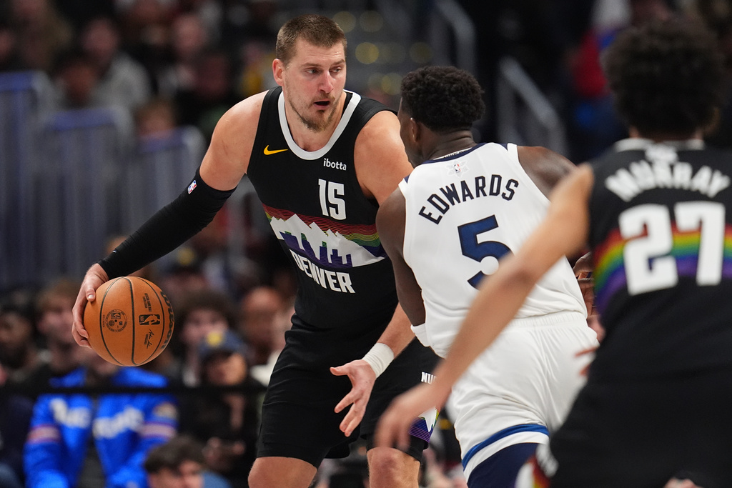 Denver Nuggets center Nikola Jokić, back, looks to pass the ball as Minnesota Timberwolves guard Anthony Edwards defends in overtime of an NBA basketball game Thursday, Dec. 25, 2025, in Denver. (AP Photo/David Zalubowski)