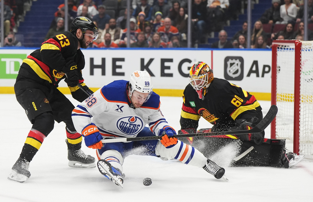 Edmonton Oilers' Andrew Mangiapane (88) is checked by Vancouver Canucks' Max Sasson (63) in front of goaltender Nikita Tolopilo (60) during the first period of an NHL hockey game in Vancouver, on Saturday, Jan. 17, 2026. (Darryl Dyck/The Canadian Press via AP)