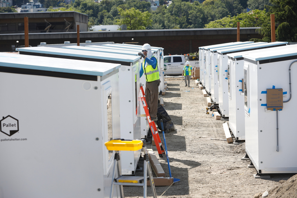 A worker inspects the top of a Pallet Shelter unit being installed in Seattle on Thursday, May 28, 2026. The single-bed units, made of composite panels, are part of Seattle Mayor Katie Wilson's plan to expand shelter for the city's homeless. (AP Photo/Manuel Valdes)