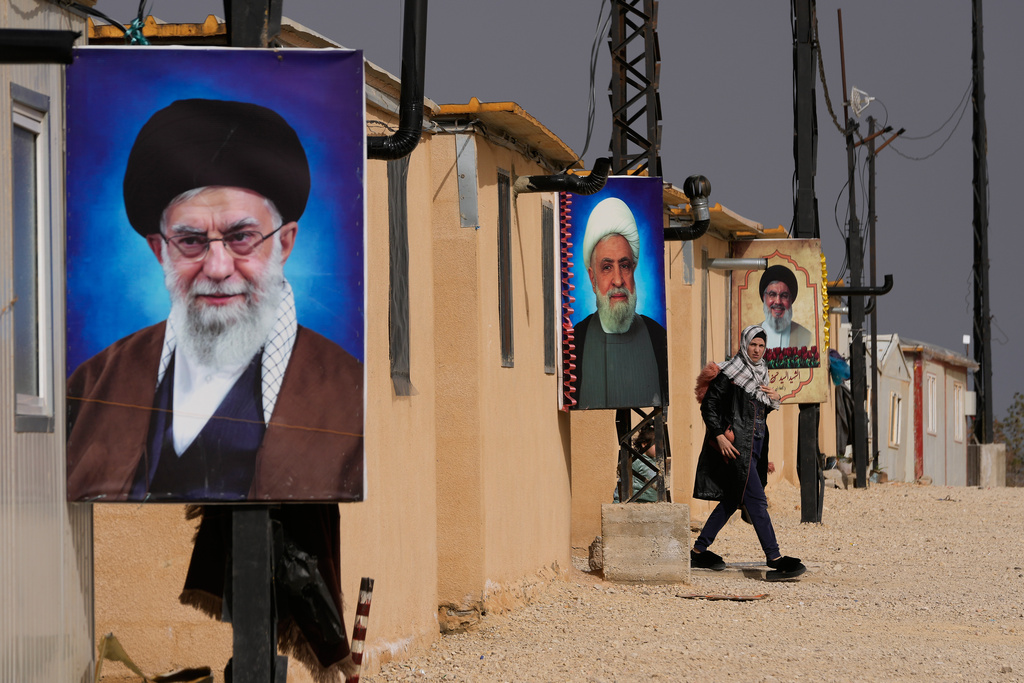 A Syrian Shiite woman walks next of portraits of Iranian Supreme Leader Ayatollah Ali Khamenei, foreground, Hezbollah leader Sheikh Naim Kassem, centre, and the late Hezbollah leader Sayyed Hassan Nasrallah, background, at the Imam Ali Housing Compound, where hundreds of mostly Lebanese and Syrian Shiite Muslims displaced from Syria reside, in Hermel, northeast Lebanon, Friday, Jan. 30, 2026. (AP Photo/Hussein Malla)