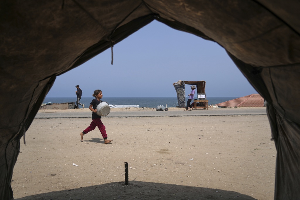 A Palestinian girl runs with an empty basin to a water distribution point during a hot summer day with temperatures reaching 36 °C (97 °F) in Deir al-Balah, in the central Gaza Strip, Wednesday, Aug. 13, 2025. The youth behind her pulls containers of water. (AP Photo/Abdel Kareem Hana)