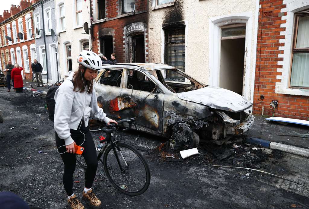 A woman walks past burnt out houses after rioting broke out late Tuesday, in east Belfast, Northern Ireland, Wednesday, June 10, 2026, following a stabbing incident. (AP Photo/Peter Morrison)