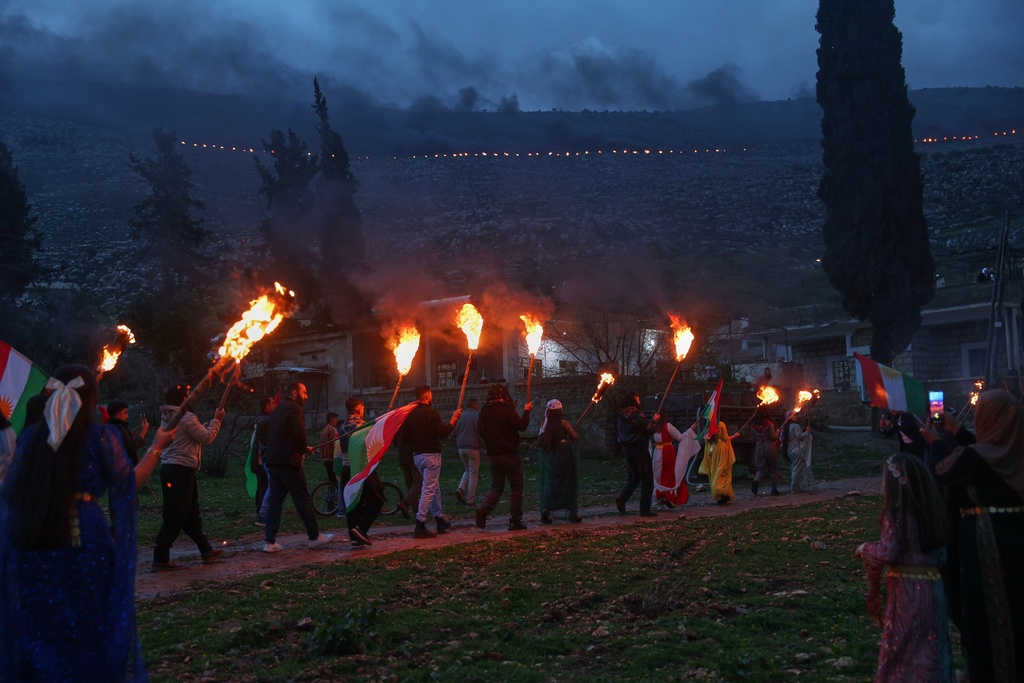 Syrian Kurds hold lit torches and Kurdish flags as they celebrate Nowruz, the Persian New Year, in the village of Basuta in the Afrin countryside, Syria, Friday, March 20, 2026. (AP Photo/Ghaith Alsayed)