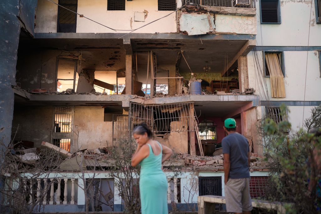 Residents look at a damaged apartment complex that neighbors say was hit during U.S. strikes to capture Venezuelan President Nicolás Maduro, in Catia La Mar, Venezuela, Sunday, Jan. 4, 2026. (AP Photo/Matias Delacroix)