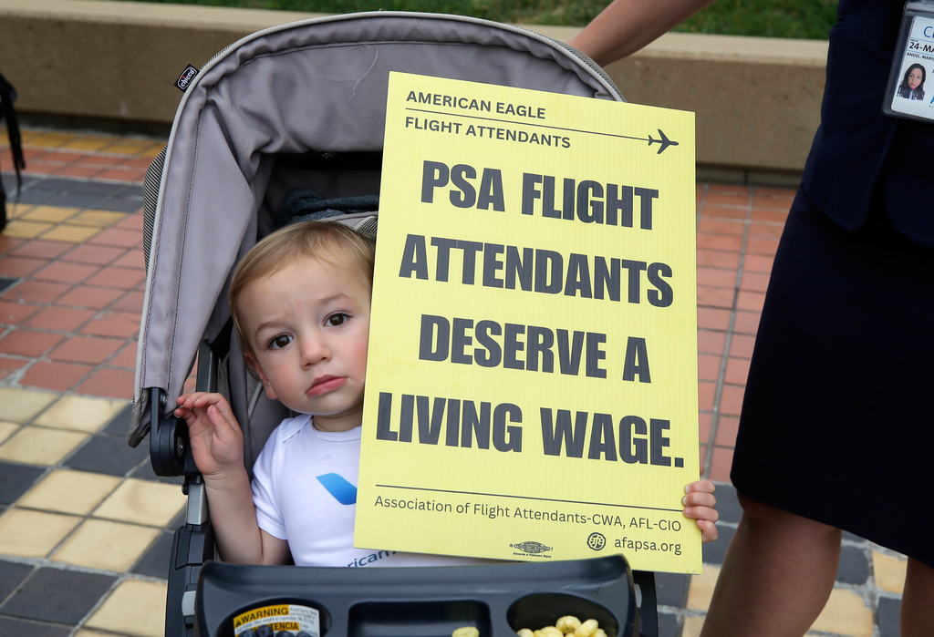 A child is seen with a placard as PSA Airlines flight attendants hold a demonstration at Ronald Reagan Washington National Airport, Monday, August 18, 2025, in Washington. (AP Photo/Rahmat Gul)