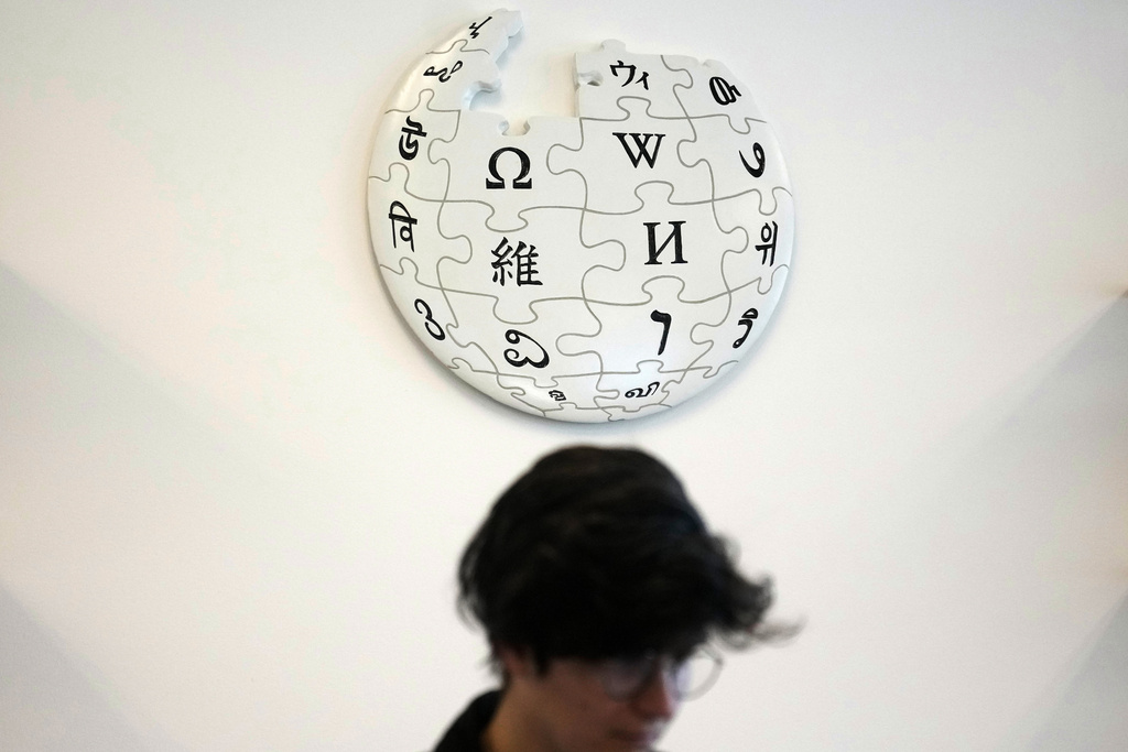 Emeline Brule, volunteer Wikipedia editor, sits below a Wikipedia logo displayed at the Wikimedia Foundation office in San Francisco, Monday, Jan. 12, 2026. (AP Photo/Jeff Chiu)