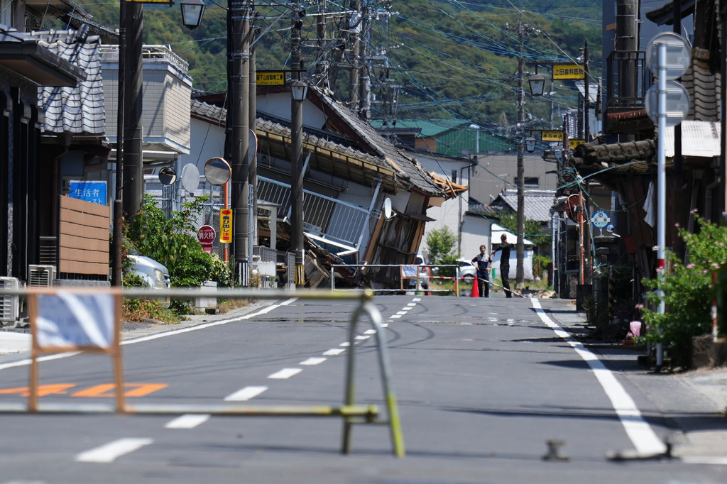 People gather by a damaged house in Hikawa, southern Japan, Friday, July 31, 2026, three days after an earthquake hit the area. (AP Photo/Hiro Komae)