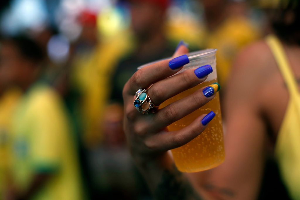 FILE - A soccer fan, with nails painted with a Brazil flag, holds a beer while watching the team's World Cup match against Serbia on a screen set up in the Rocinha favela in Rio de Janeiro, Brazil, Nov. 24, 2022. (AP Photo/Bruna Prado, File)