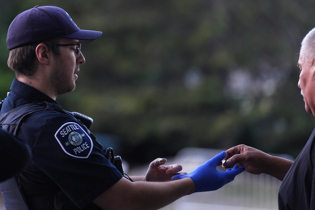 A vendor, right, who found a bullet casing, gives it to a police officer after a shooting at Seattle Center during the Bite of Seattle food festival, Monday, July 27, 2026, in Seattle. (AP Photo/Lindsey Wasson)