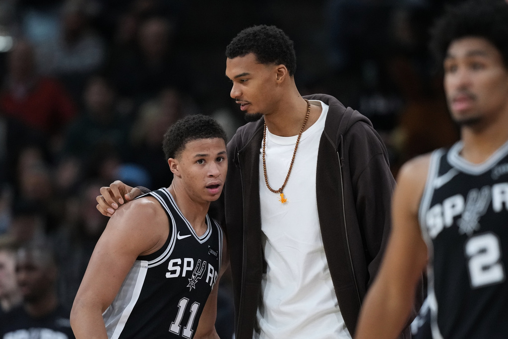 San Antonio Spurs forward Victor Wembanyama, center, talks with teammate forward Carter Bryant (11) during the first half of an NBA basketball game against the Memphis Grizzlies in San Antonio, Tuesday, Dec. 2, 2025. (AP Photo/Eric Gay)
