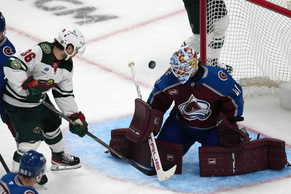 Minnesota Wild right wing Mats Zuccarello, left, redirects the puck at Colorado Avalanche goaltender Scott Wedgewood in the third period of Game 1 of an NHL hockey Stanley Cup second-round playoff series Sunday, May 3, 2026, in Denver. (AP Photo/David Zalubowski)