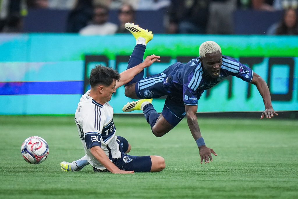 Sporting Kansas City's Capita, right, falls after having the ball stripped away by Vancouver Whitecaps' Andres Cubas, left, during the first half of an MLS soccer match in Vancouver, British Columbia, Friday, April 17, 2026. (Darryl Dyck/The Canadian Press via AP)