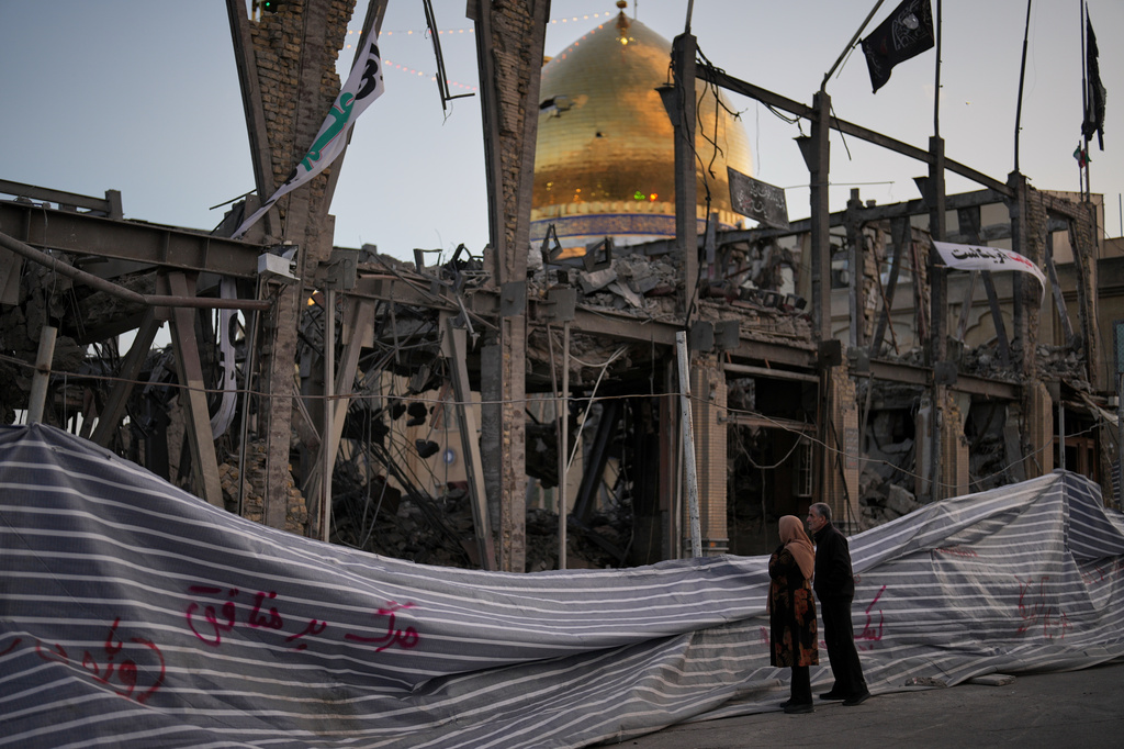 Pedestrians look at a destroyed building within the Grand Hosseiniyeh, with the mosque visible in the background, which officials at the site say was hit by U.S.-Israeli airstrikes Tuesday, in Zanjan, Iran, Saturday, April 4, 2026. (AP Photo/Francisco Seco)