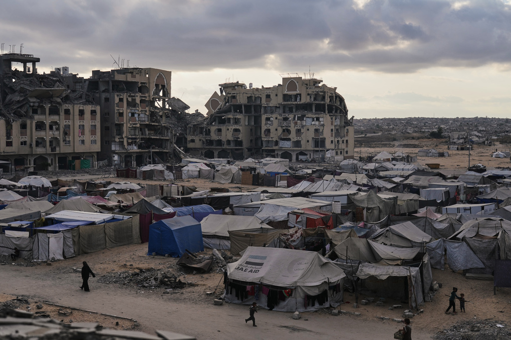 A tent camp for displaced Palestinians sits adjacent to destroyed homes and buildings in Khan Younis, Gaza Strip, Saturday, Oct. 18, 2025. (AP Photo/Jehad Alshrafi)
