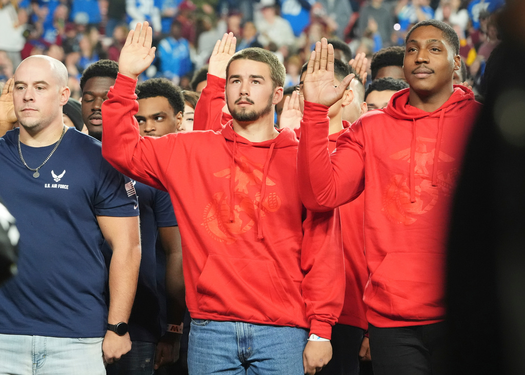 New recruits stand during the Oath of Enlistment delivered by President Donald Trump during an NFL football game between the Washington Commanders and the Detroit Lions at Northwest Stadium in Landover, Md., Sunday, Nov. 9, 2025. (AP Photo/Jacquelyn Martin)