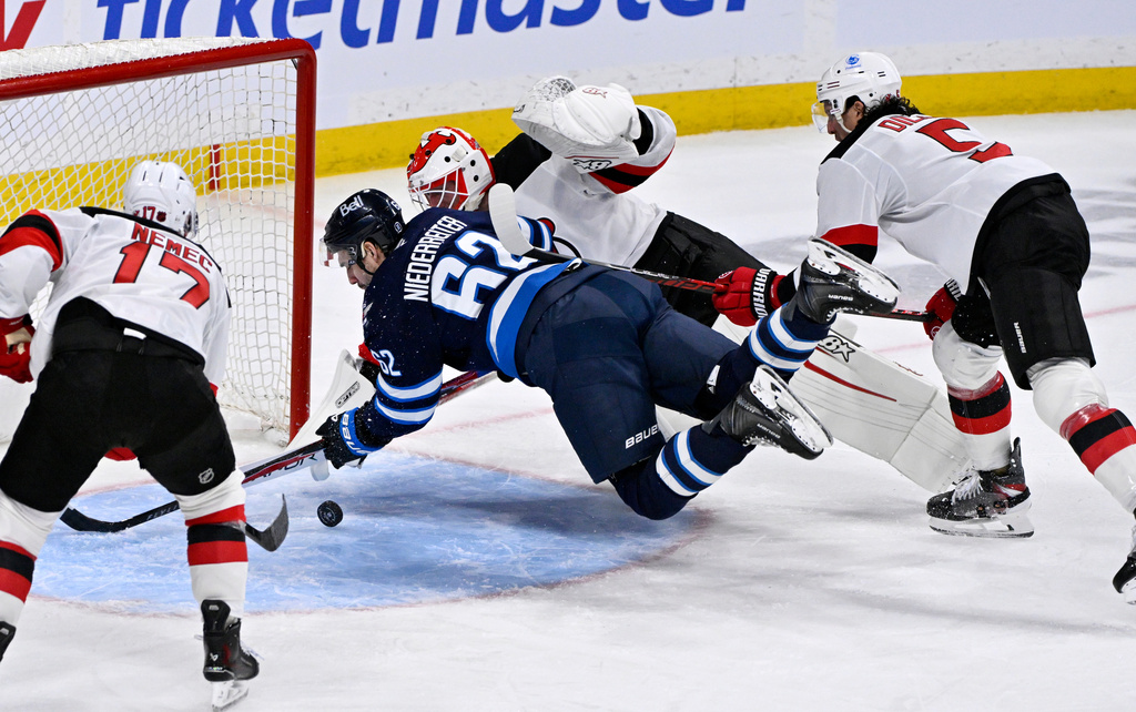Winnipeg Jets' Nino Niederreiter (62) tries to control the puck as New Jersey Devils goaltender Jake Allen, center top, makes a save during third-period NHL hockey game action in Winnipeg, Manitoba, Sunday, Jan. 11, 2026. (Fred Greenslade/The Canadian Press via AP)
