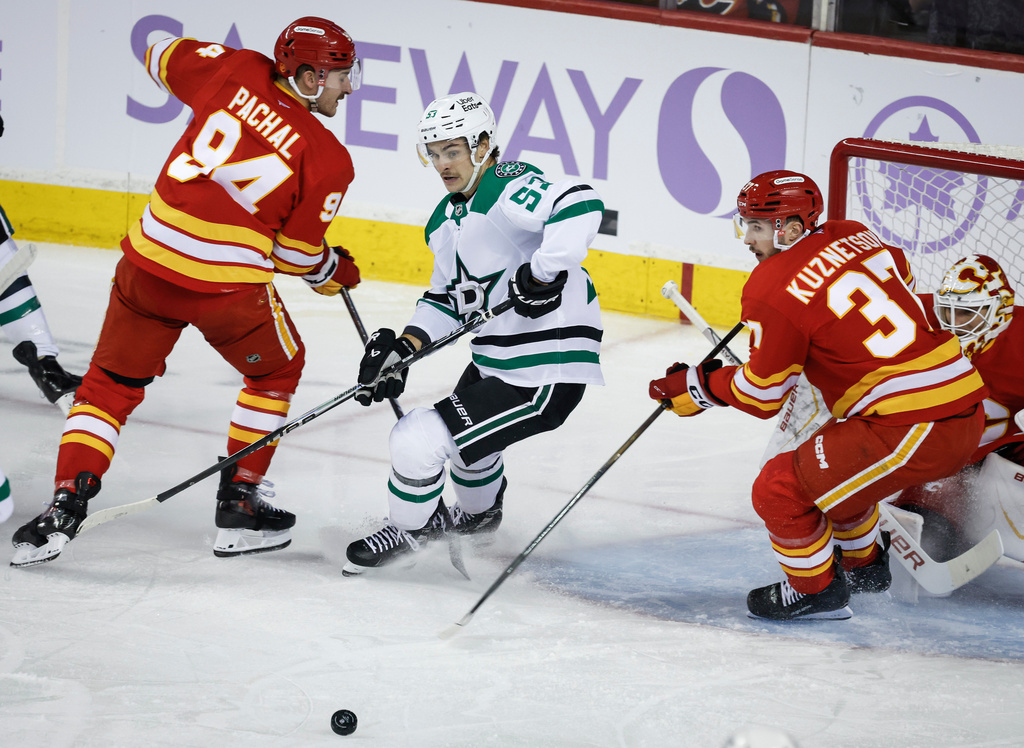 Dallas Stars' Wyatt Johnston, centre, chases a loose puck as Calgary Flames' Brayden Pachal, left, and Yan Kuznetsov defend during first period NHL hockey action in Calgary on Saturday, Nov. 22, 2025. (Jeff McIntosh/The Canadian Press via AP)