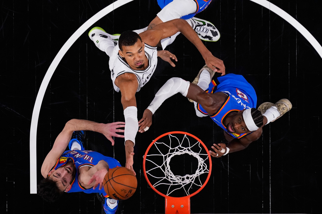 San Antonio Spurs forward Victor Wembanyama (1) drives to the basket against Oklahoma City Thunder center Chet Holmgren (7) and guard Shai Gilgeous-Alexander (2) during the first half in Game 4 in the Western Conference finals NBA basketball playoffs series in San Antonio, Sunday, May 24, 2026. (AP Photo/Eric Gay)