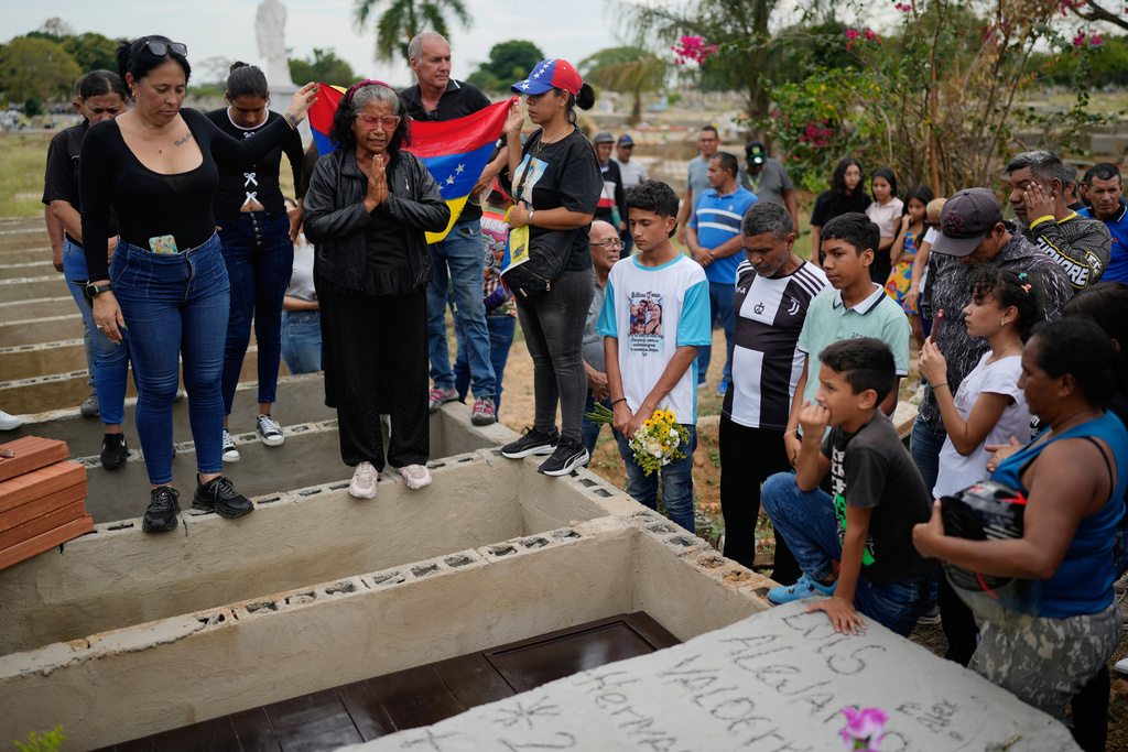 Relatives of Edilson Torres, a Venezuelan police officer who died in prison a month after being arrested on accusations of treason, gather around his grave during his funeral in Guanare, Venezuela, Tuesday, Jan. 13, 2026. (AP Photo/Ariana Cubillos)
