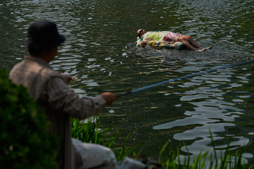 A view of a man fishing as a resident swims along the Liangmahe river, in Beijing, Tuesday, May 12, 2026. (AP Photo/Andy Wong)