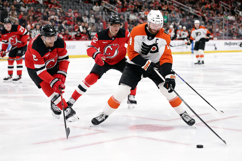 Philadelphia Flyers center Sean Couturier (14) controls the puck in front of New Jersey Devils defenseman Johnathan Kovacevic (8) and Nick Bjugstad (72) during the first period of an NHL hockey game Tuesday, April 7, 2026, in Newark, N.J. (AP Photo/Adam Hunger)