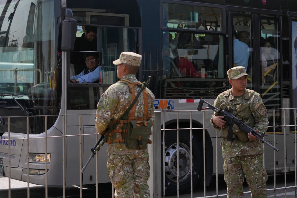 A bus driver peers through his window at soldiers standing guard at a bus stop in Lima, Peru, Wednesday, Oct. 22, 2025, after President Jose Jeri declared a state of emergency. (AP Photo/Martin Mejia)