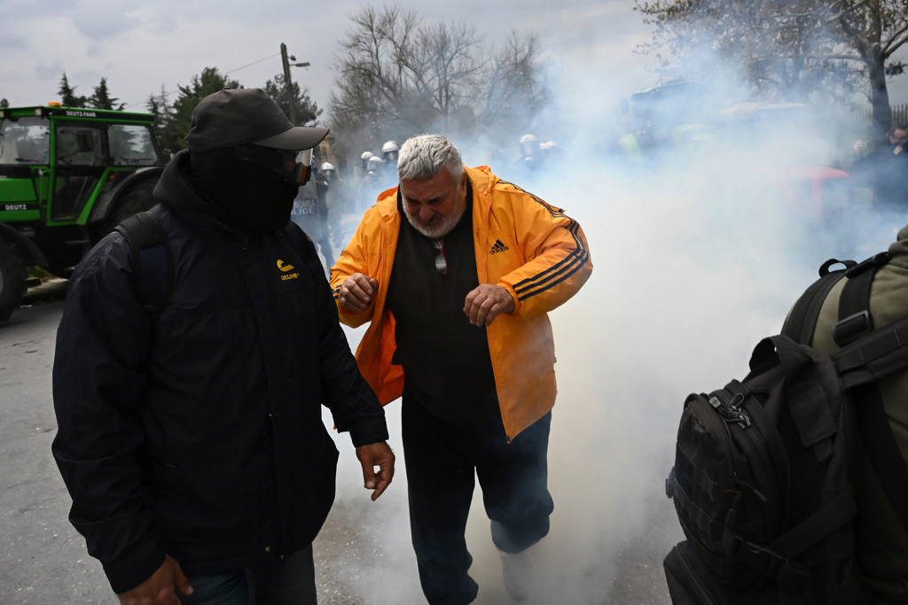 A man runs to avoid tear gas during clashes with riot police after farmers tried to block the main access road to Thessaloniki's international airport, northern Greece, on Friday, Dec. 5, 2025, as protests over delays in European Union-backed agricultural subsidy payments escalated. (AP Photo/Giannis Papanikos)