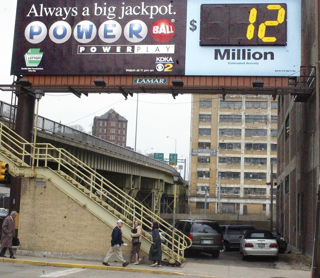 FILE - People move along the sidewalk at lunchtime in Pittsburgh in front of a billboard advertising the current Powerball Jackpot on Monday, March 21, 2005. (AP Photo/Keith Srakocic, File)