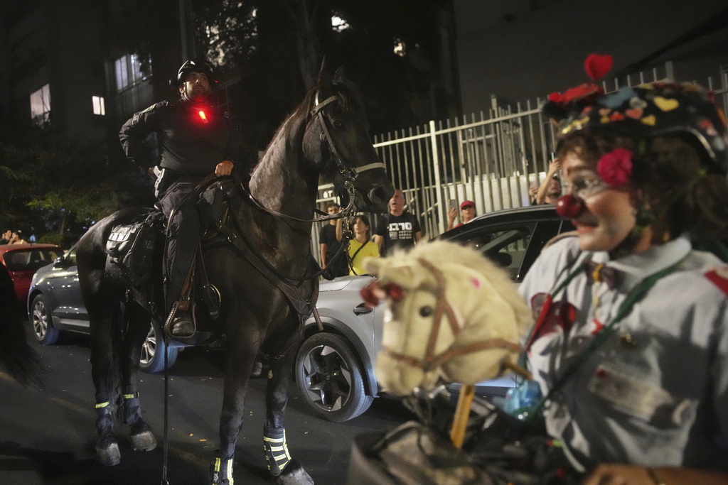 An Israeli mounted police officer rides next the performer clown Hashoteret Az-Oolay during a protest demanding the immediate release of hostages held by Hamas and calling for the Israeli government to reverse its decision to take over Gaza City and other areas in the Gaza Strip, in Tel Aviv, Israel, Sunday, Aug. 17, 2025. (AP Photo/Ohad Zwigenberg)