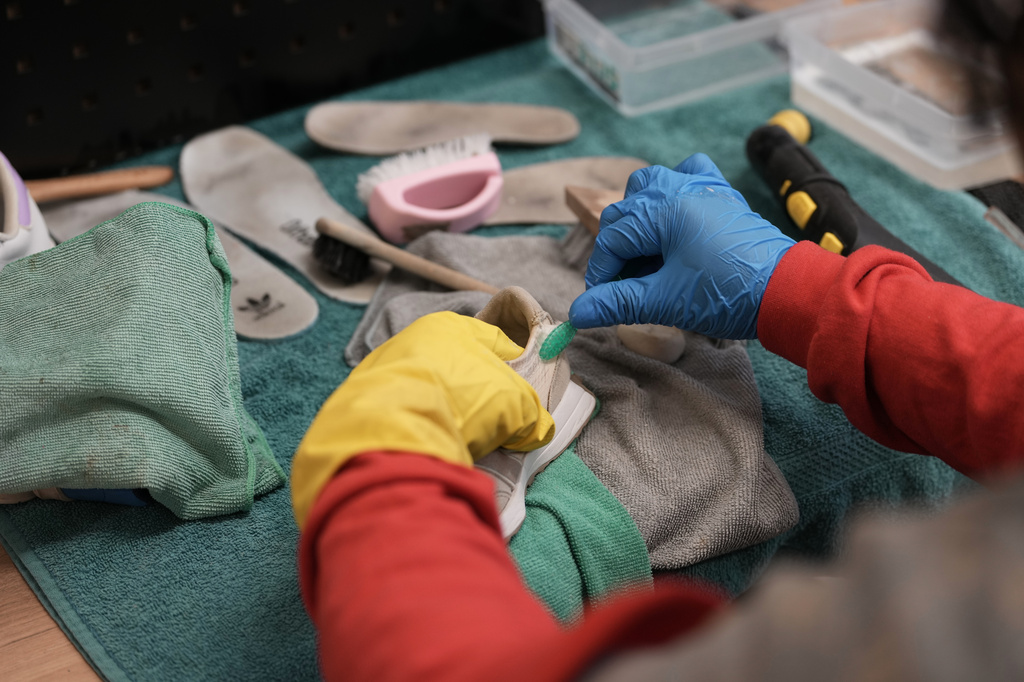 A worker uses a toothbrush to clean a used sneaker at SneakCoeurZ, a nonprofit organization giving used footwear a second life, in Champs-sur-Marne, east of Paris, Wednesday, March 25, 2026. (AP Photo/Thibault Camus)