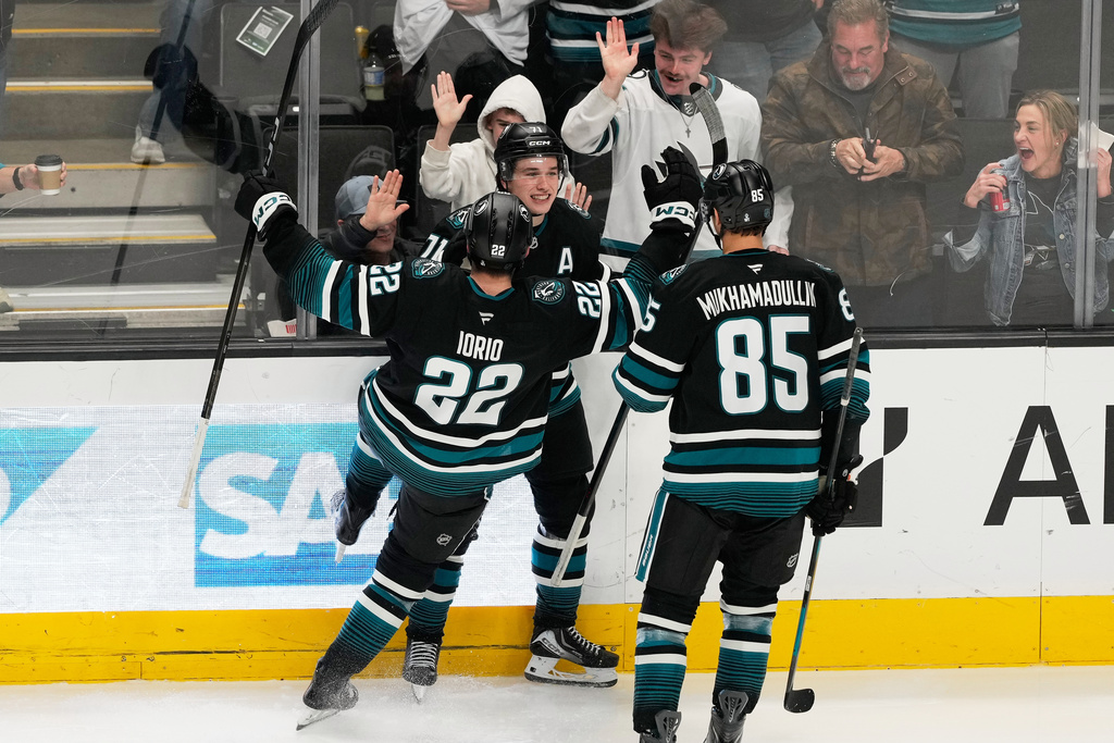 San Jose Sharks center Macklin Celebrini, middle, is congratulated by defenseman Vincent Iorio (22) and defenseman Shakir Mukhamadullin (85) after scoring against the Calgary Flames during the third period of an NHL hockey game in San Jose, Calif., Tuesday, Dec. 16, 2025. (AP Photo/Jeff Chiu)