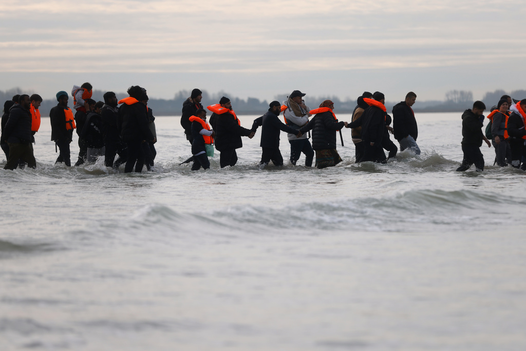 Migrants walk in the water to board a small boat in an attempt to reach Britain, Thursday, Nov. 6, 2025 in Gravelines, northern France. (AP Photo/Jean-Francois Badias)