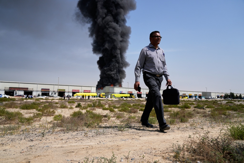 A man walks away after watching as a black plume of smoke rises from a warehouse in the industrial area of Sharjah City, United Arab Emirates, Sunday, March 1, 2026, following reports of Iranian strikes in Dubai. (AP Photo/Altaf Qadri)