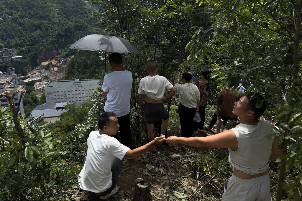 Residents standing on a hill watch rescuers using a heavy duty machine to clear rubble to search for trapped victims at the scene of a landslide in Pengshui County in southwestern China's Chongqing on Sunday, July 19, 2026. (AP Photo/Andy Wong)