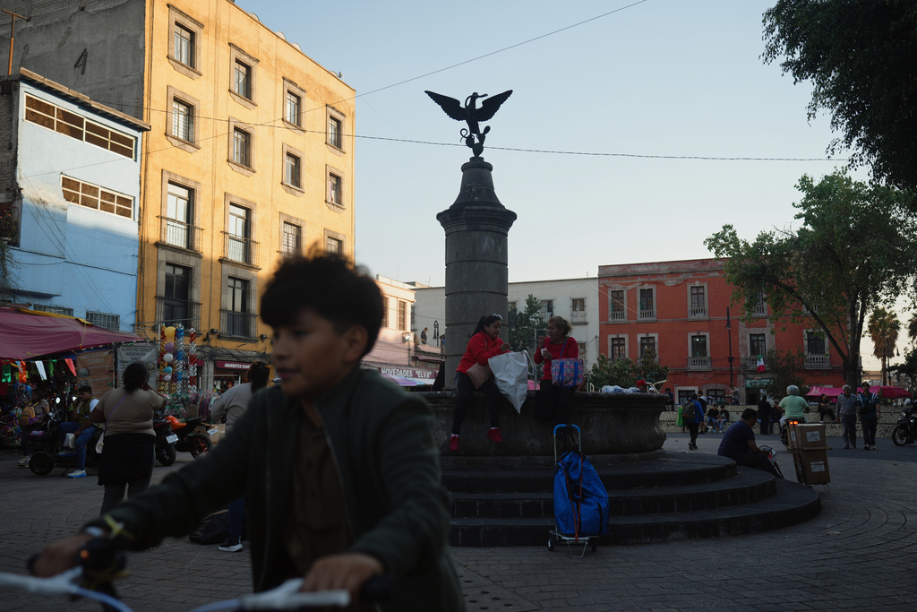 People at the square of Aguilita in Mexico City walk past a central sculpture depicting Mexico's coat of arms which shows an eagle perched on a cactus devouring a rattlesnake, Thursday, Nov. 13, 2025. (AP Photo/Claudia Rosel)