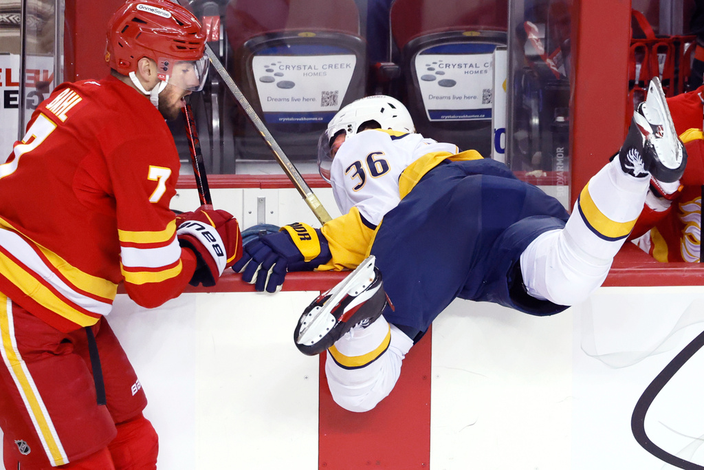 Nashville Predators' Cole Smith, right, is knocked over the boards by Calgary Flames' Kevin Bahl during the second period of an NHL hockey game in Calgary, Alberta, Saturday, Jan. 3, 2026. (Larry MacDougal/The Canadian Press via AP)