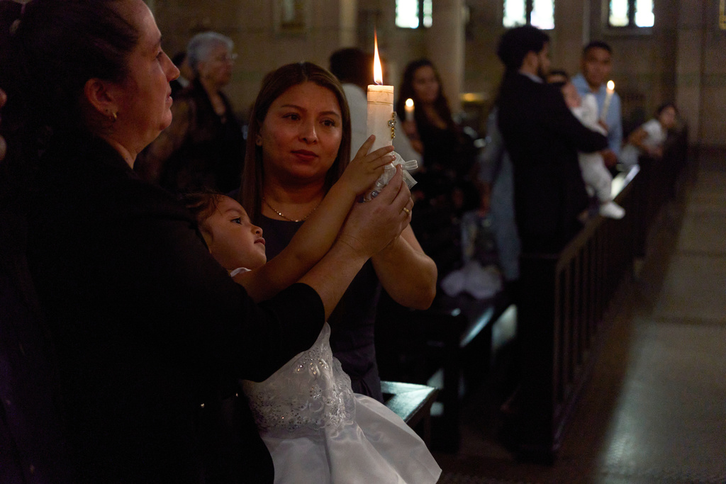 Parishioners hold a candle during a baptism at the Shrine of the Sacred Heart Catholic church in Washington, Oct. 11, 2025. (AP Photo/Luis Andres Henao)