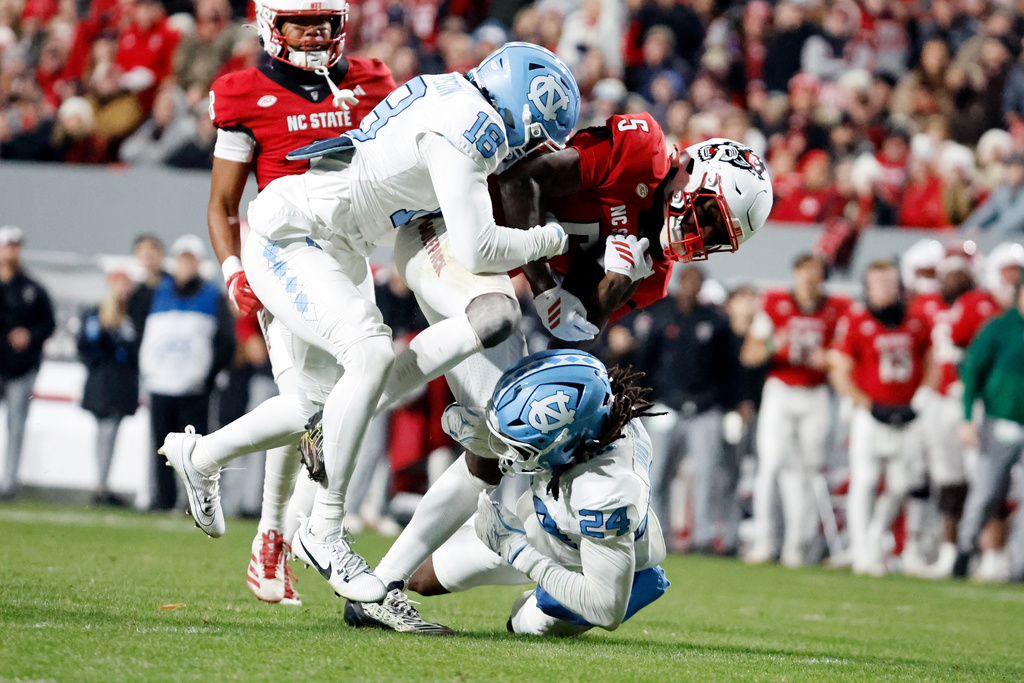 North Carolina State's Noah Rogers (5) is tackled by North Carolina's Javion Butts (24) and Jaiden Patterson (18) during the first half of an NCAA college football game in Raleigh, N.C., Saturday, Nov. 29, 2025. (AP Photo/Karl DeBlaker)